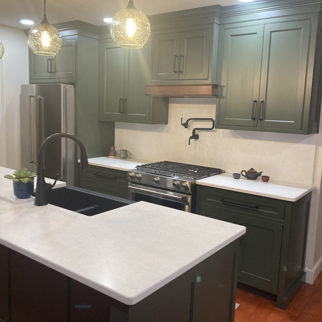 Classic kitchen with green painted cabinets, white countertop, and black hardware.